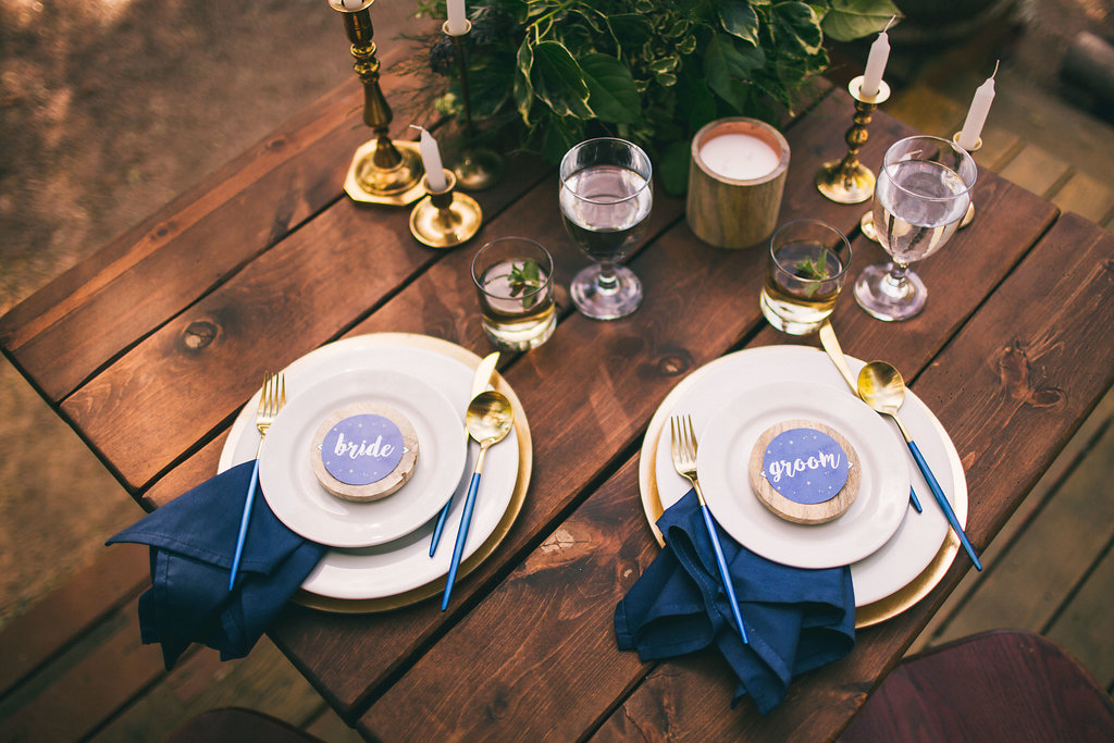 Bride and Groom place setting with navy napkins and gold silverware and wood table