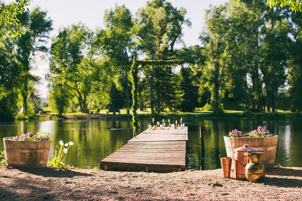 ceremony site with lake, copper accents, greenery arch and a bunch of tapper candle sticks