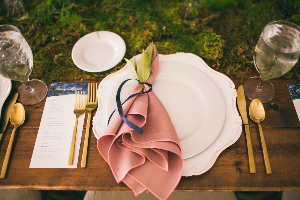 place setting with white plate, gold flatware and moss