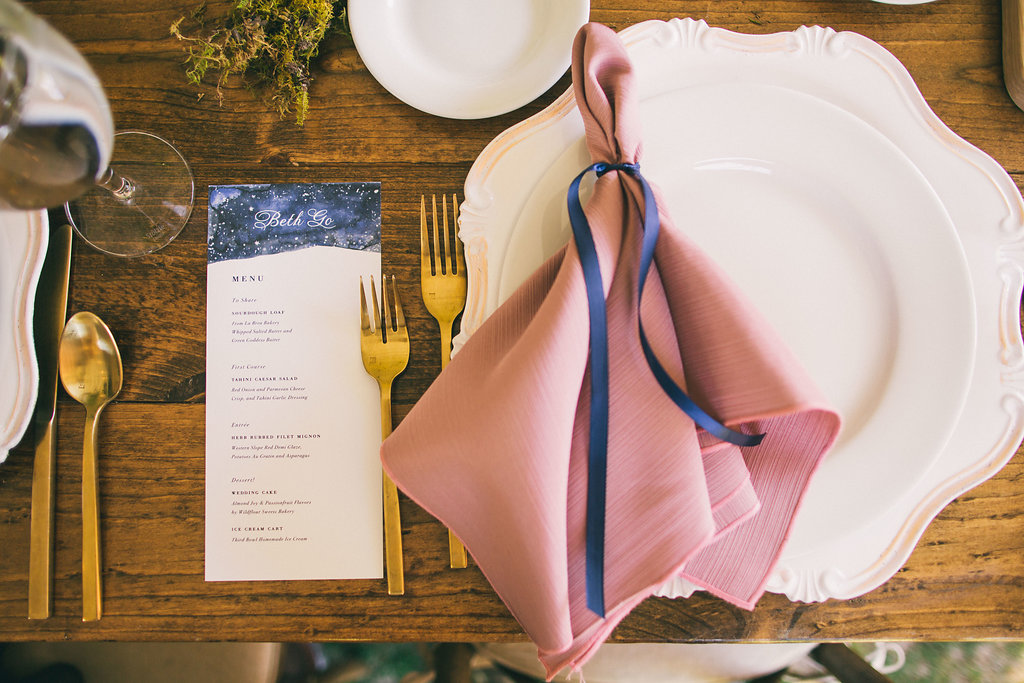 place setting with white charger, gold flatware and pink napkin